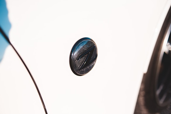 A close-up shot of a car emblem on a white vehicle. The emblem is circular with a dark metallic finish and features a distinctive 'Z' design in the center.