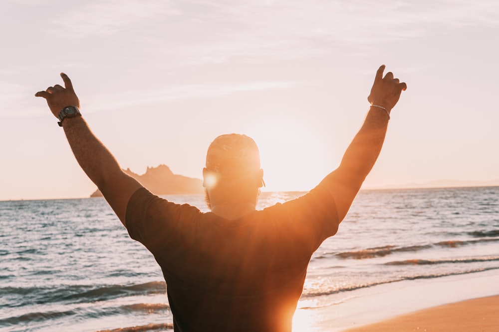 man in black shirt raising his hands on beach during daytime