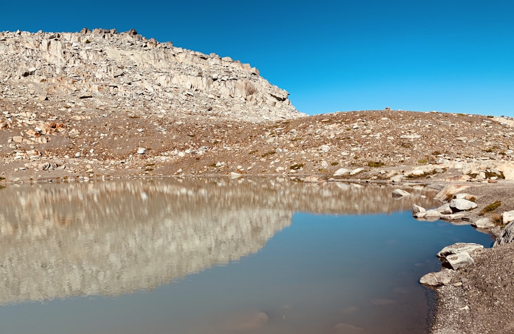 brown and white rocky mountain beside body of water under blue sky during daytime