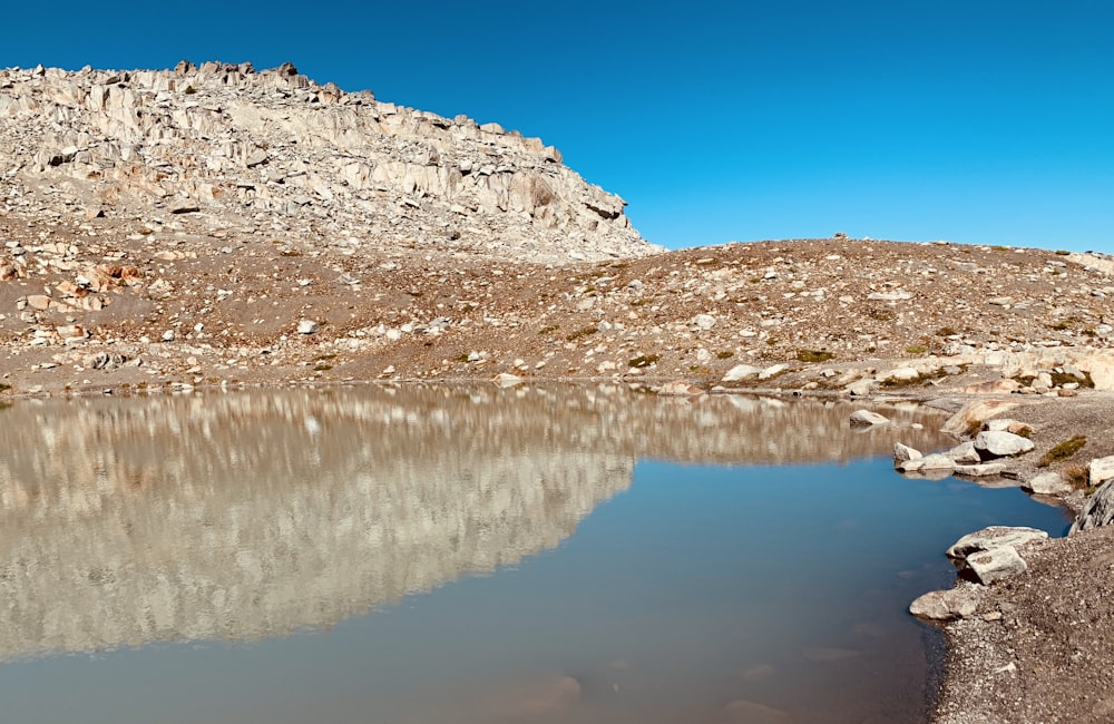 montagna rocciosa marrone e bianca accanto allo specchio d'acqua sotto il cielo blu durante il giorno