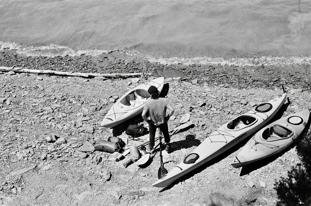 grayscale photo of man in black jacket and pants holding surfboard on field