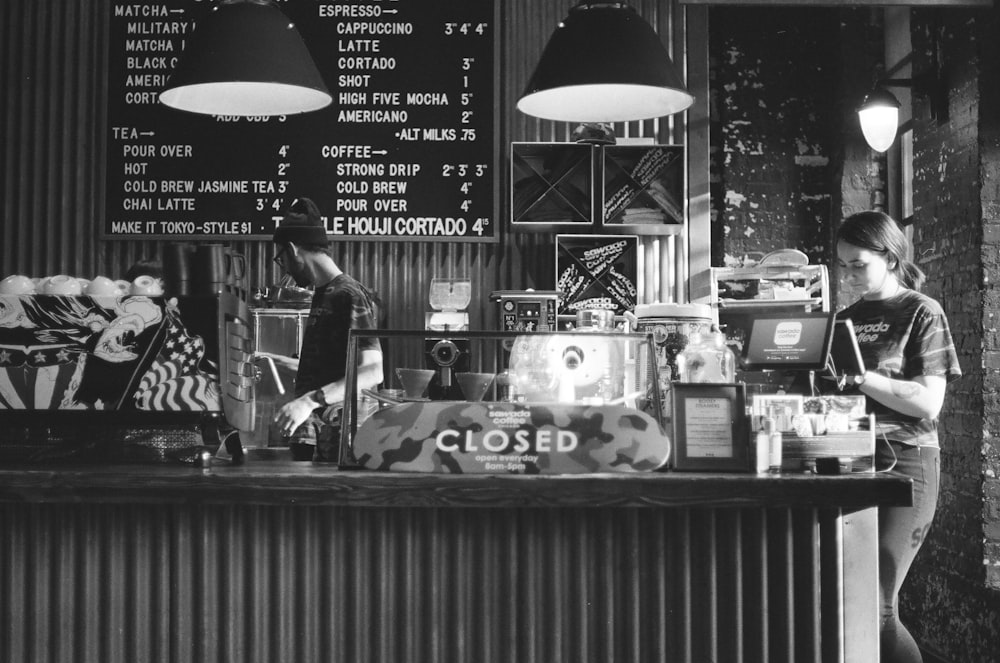 grayscale photo of man in black t-shirt standing near counter