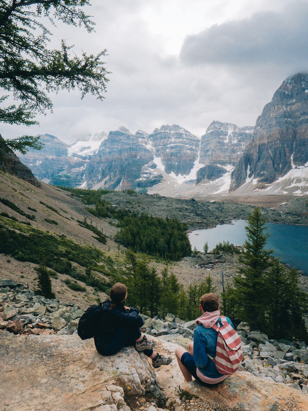 man in red jacket sitting on rock near lake and mountain range