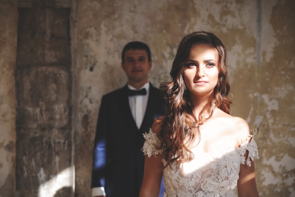 man in black suit jacket beside woman in white floral lace sleeveless dress