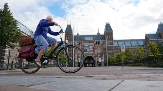 woman in blue long sleeve shirt riding on black bicycle during daytime in Rijksmuseum Netherlands