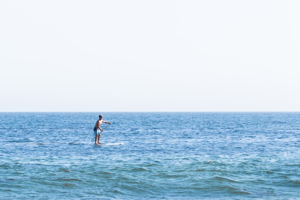 woman in blue bikini standing on white surfboard on sea during daytime