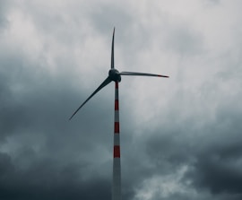 A technician inspecting a tall wind turbine against a cloudy sky.