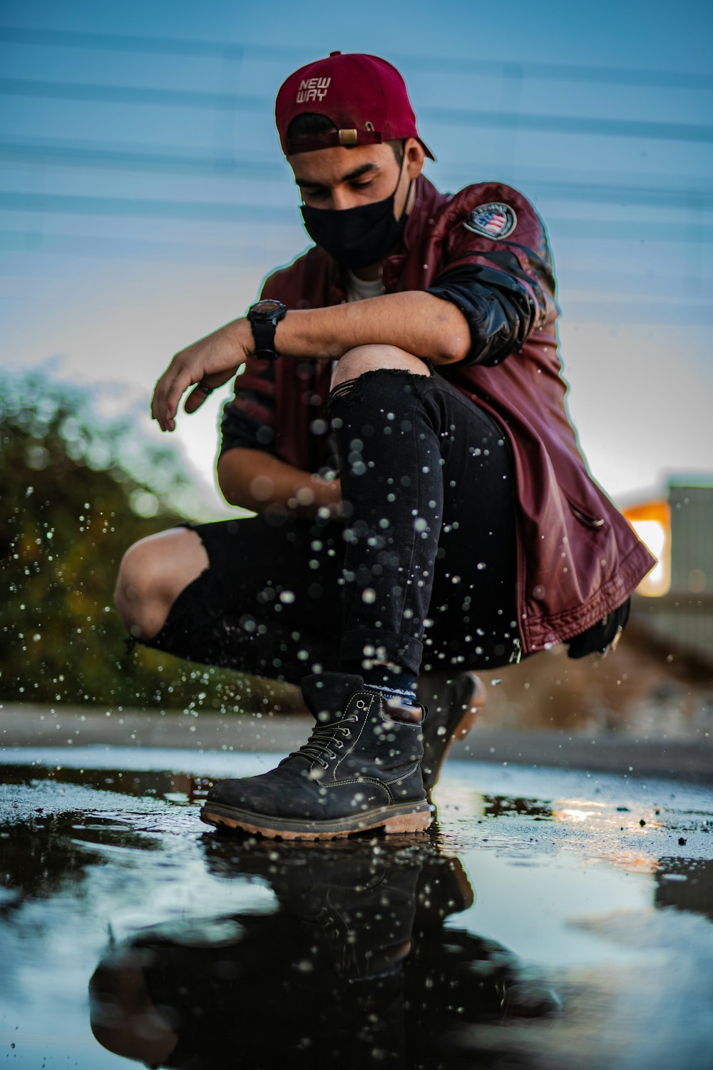 woman in black and white floral pants and black boots sitting on rock near body of during