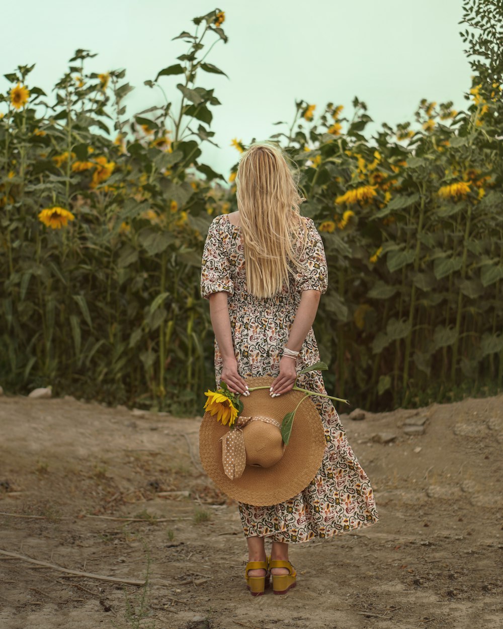 a woman in a dress and hat standing in a field of sunflowers