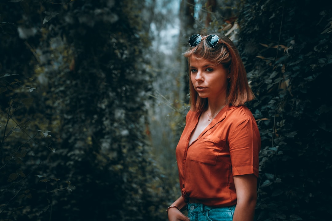 woman in red button up shirt and blue denim shorts standing in forest during daytime