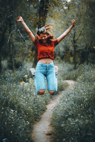 woman in orange t-shirt and blue denim jeans standing on green grass field during daytime