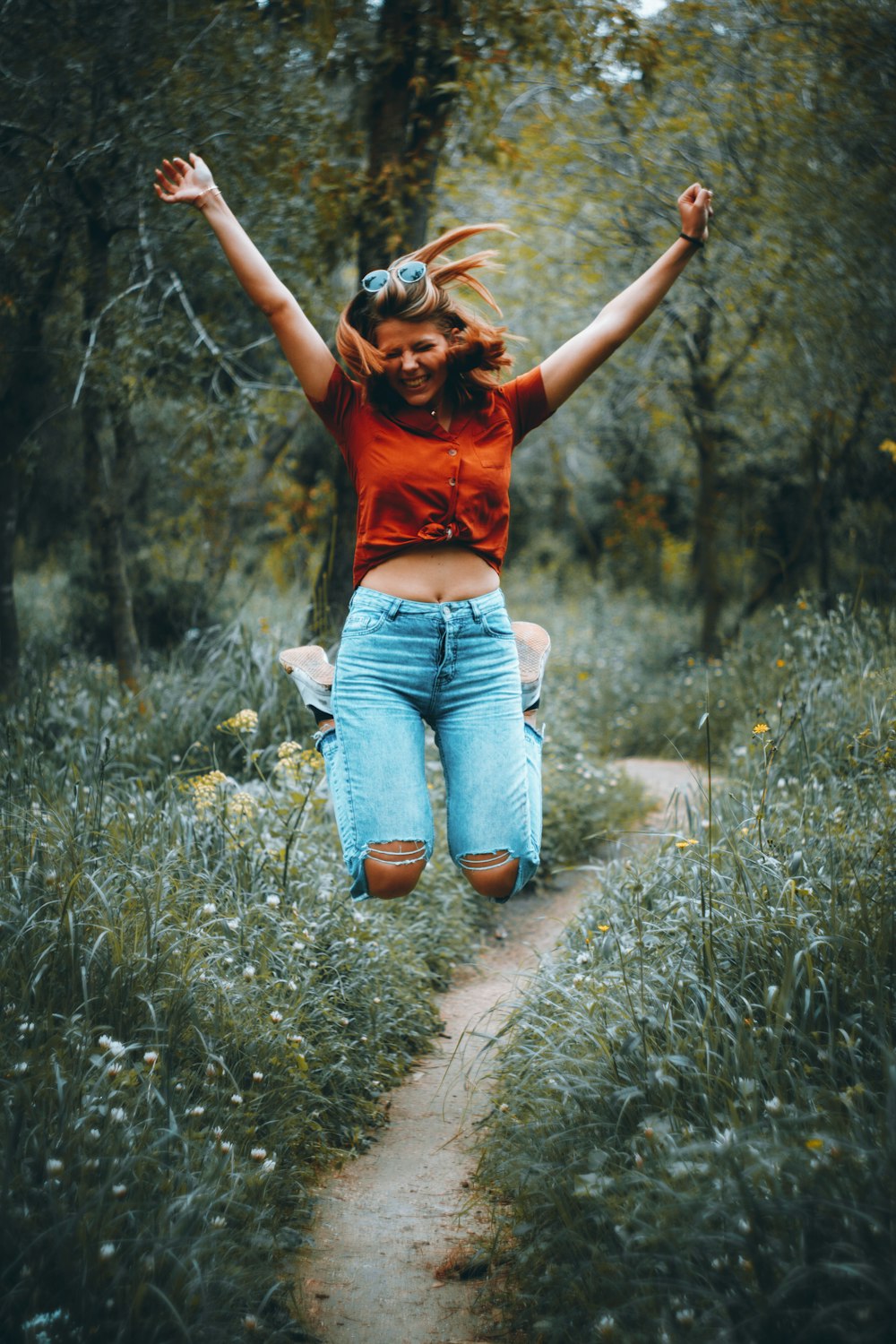 woman in orange t-shirt and blue denim jeans standing on green grass field during daytime