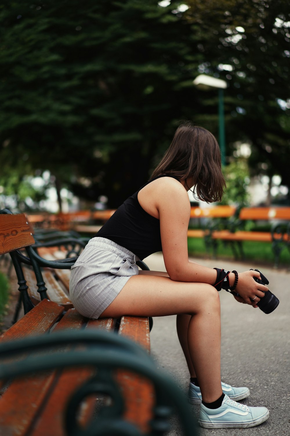 woman in black tank top and white shorts sitting on brown wooden bench holding black dslr