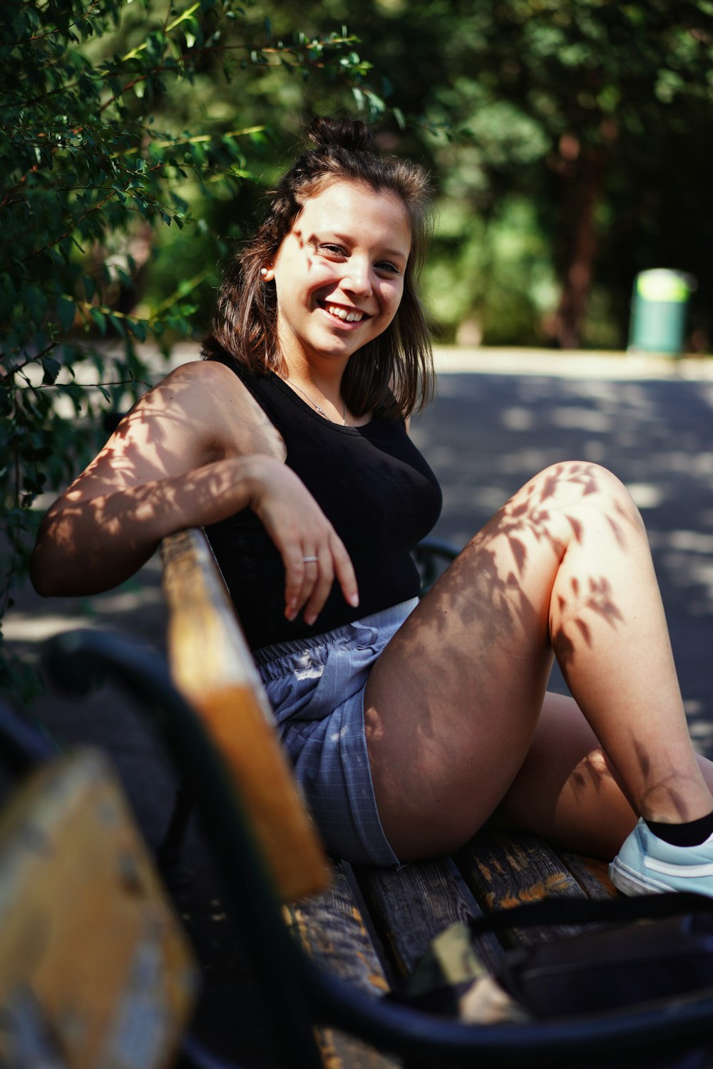woman in black shirt and blue denim shorts sitting on brown wooden bench