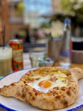 A rustic wooden table set with a steaming khachapuri, a plate of khinkali dumplings, and a glass of deep red Georgian wine, bathed in warm light.