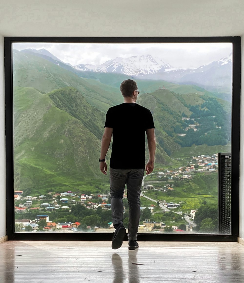 man in black t-shirt and gray denim jeans standing on brown wooden floor