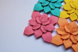 Several colorful origami flowers arranged together, crafted from paper in shades of teal, pink, yellow, and orange against a plain white background.