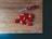 A wooden cutting board with a red-handled Swiss Army knife and nine small red tomatoes arranged on it.