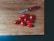 A wooden cutting board with a red-handled Swiss Army knife and nine small red tomatoes arranged on it.