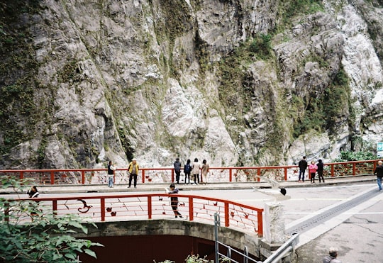 people walking on red bridge near gray mountain during daytime in Hualien City Taiwan