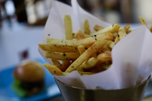 Golden crispy fries sprinkled with seasoning served in a rustic paper cone.