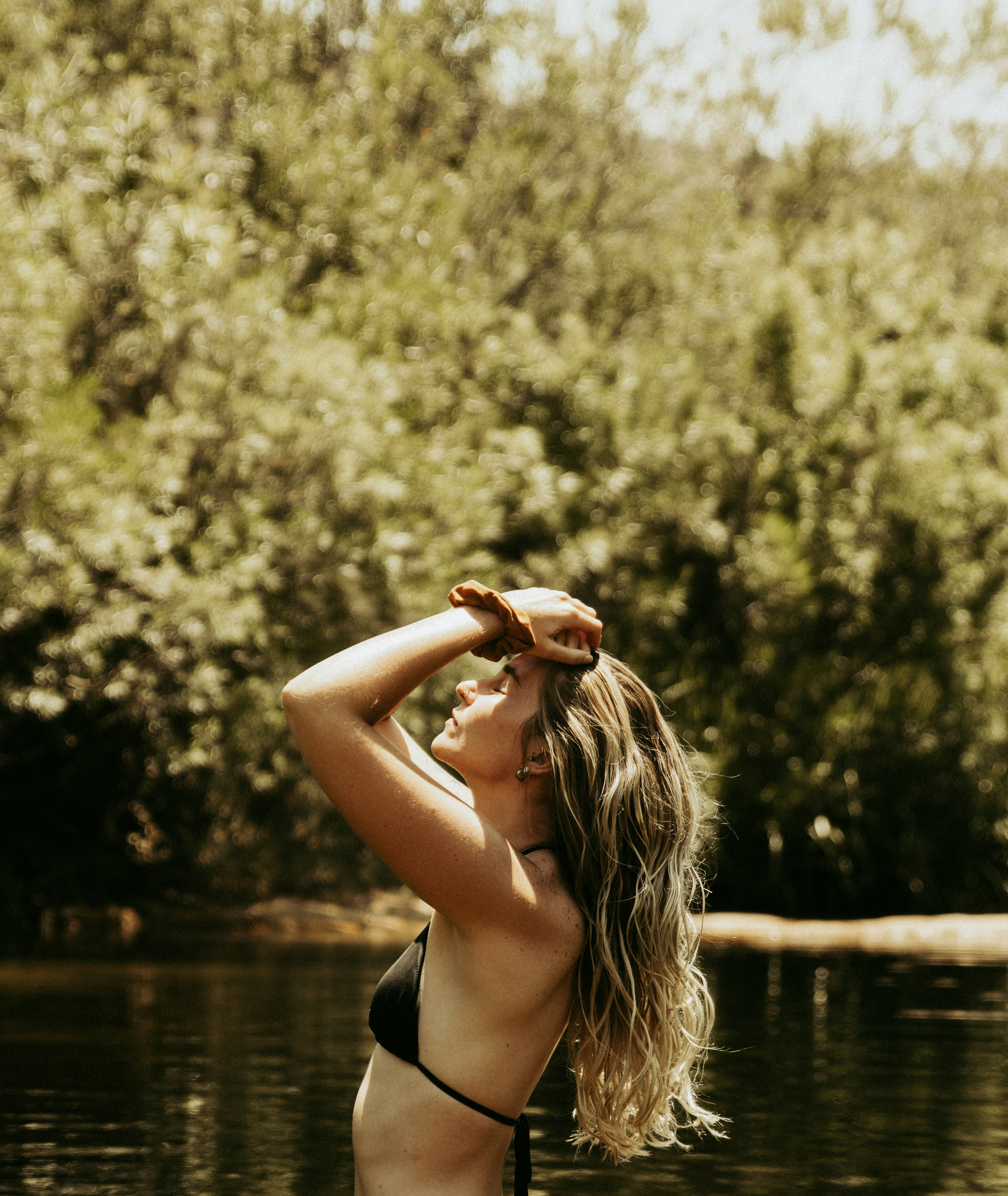 woman in black bikini top raising her right hand near body of water during daytime