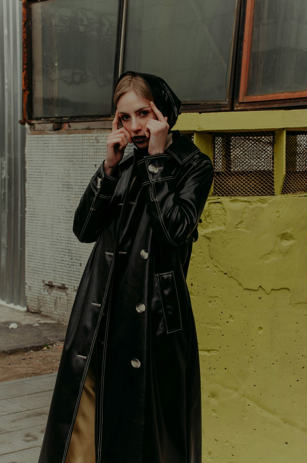 woman in black coat standing near yellow wall