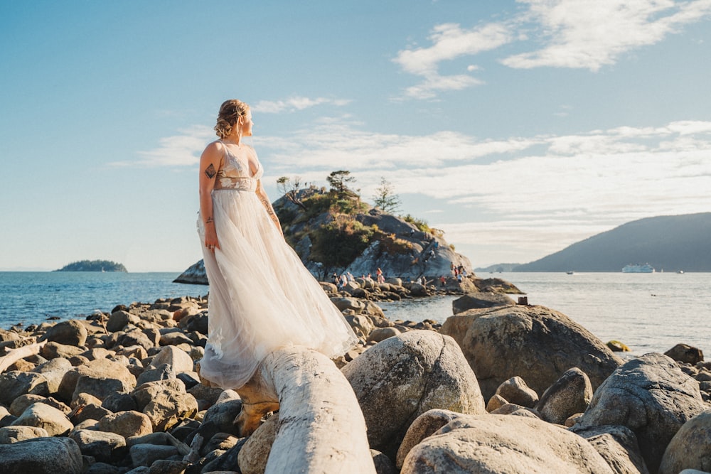woman in white wedding dress standing on rocky shore during daytime