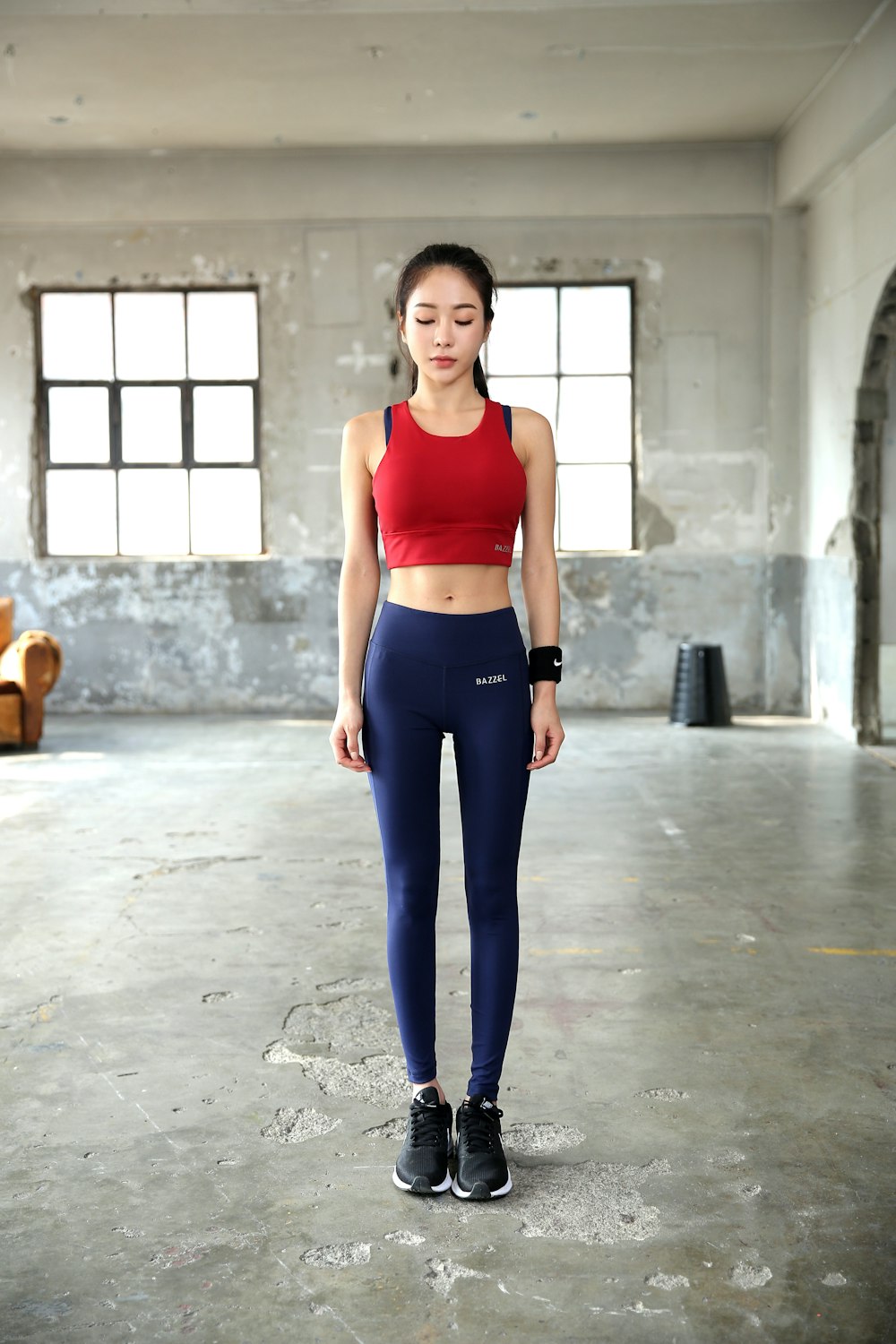 woman in red tank top and blue leggings standing on gray concrete floor