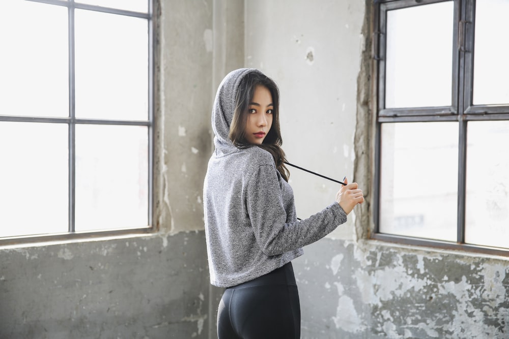 woman in gray sweater and black pants standing beside window
