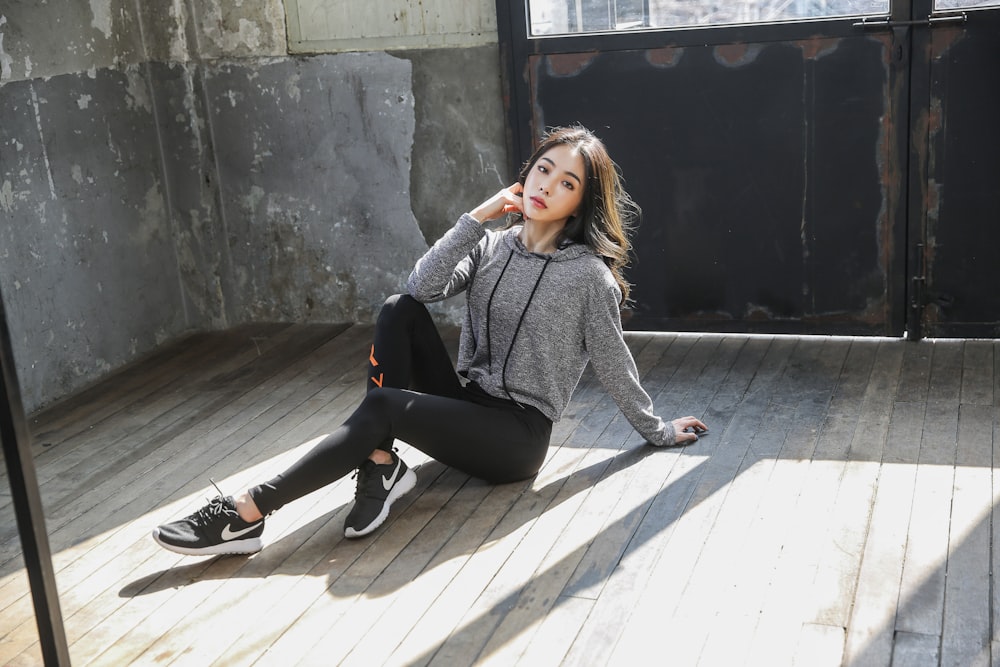 woman in gray sweater and black pants sitting on brown wooden floor