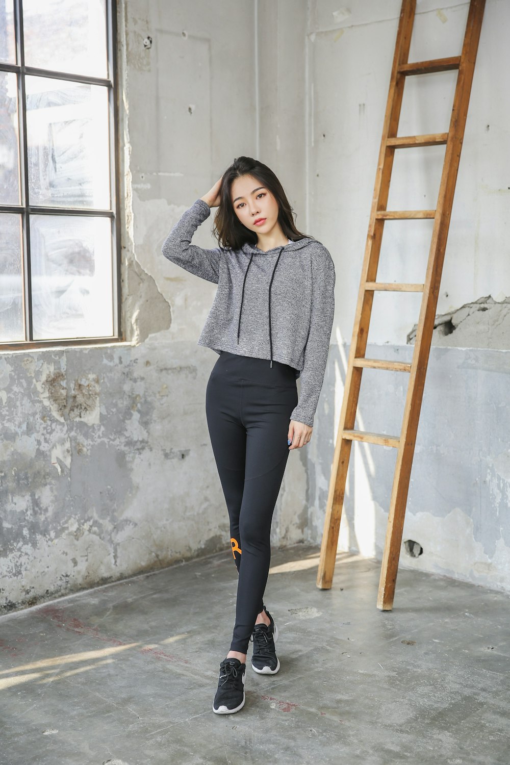 woman in gray sweater and black pants standing beside brown wooden framed glass window