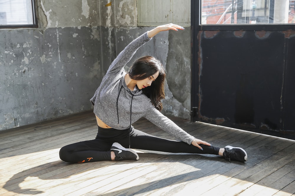 woman in gray long sleeve shirt and black pants sitting on wooden floor