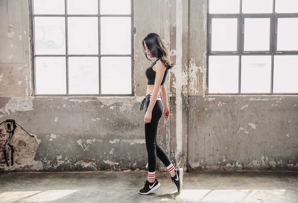 woman in black sports bra and black leggings standing beside gray concrete wall during daytime