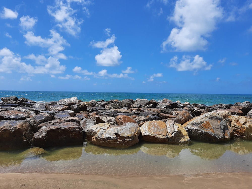 昼間の青空の下、海岸に浮かぶ茶色い岩