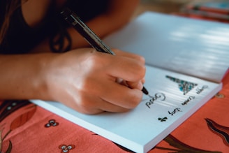 Close-up of hands holding a pen over a notebook with delicate floral decorations.