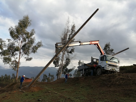 Workers installing a concrete pole at an electrical site under a bright blue sky.