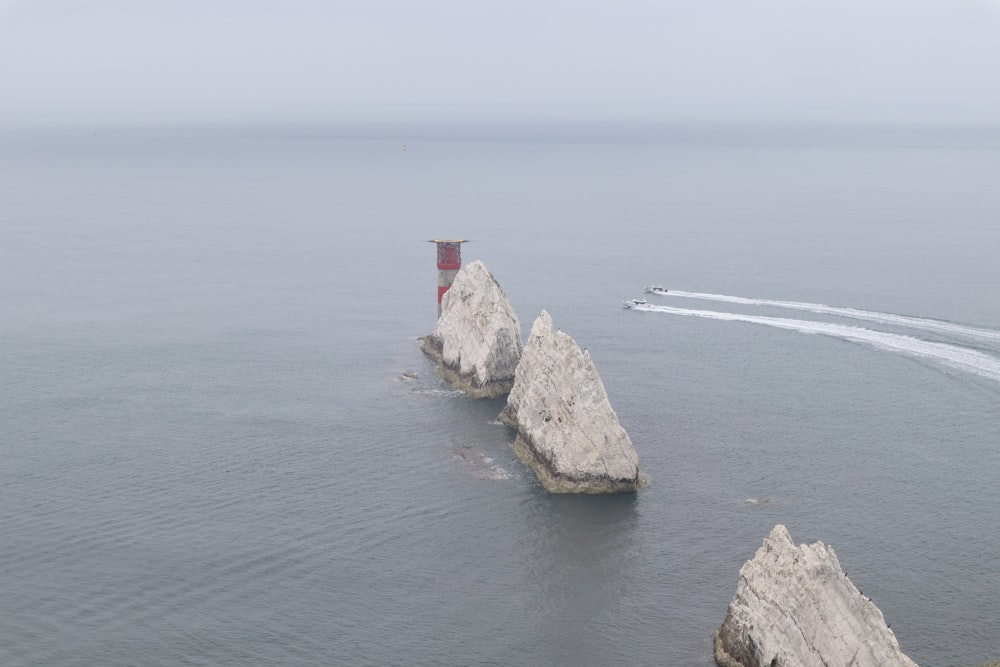 white and red lighthouse on brown rock formation near body of water during daytime