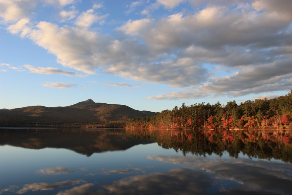 body of water near mountain under cloudy sky during daytime