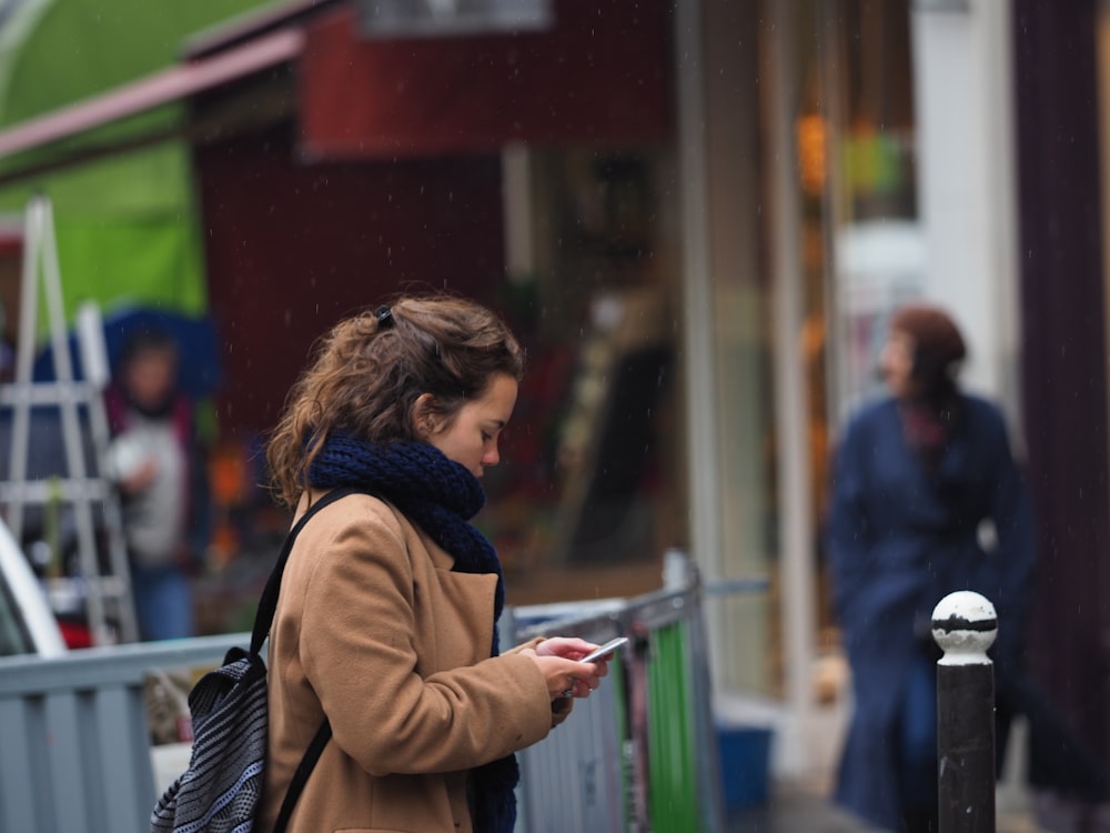 woman in brown coat using smartphone
