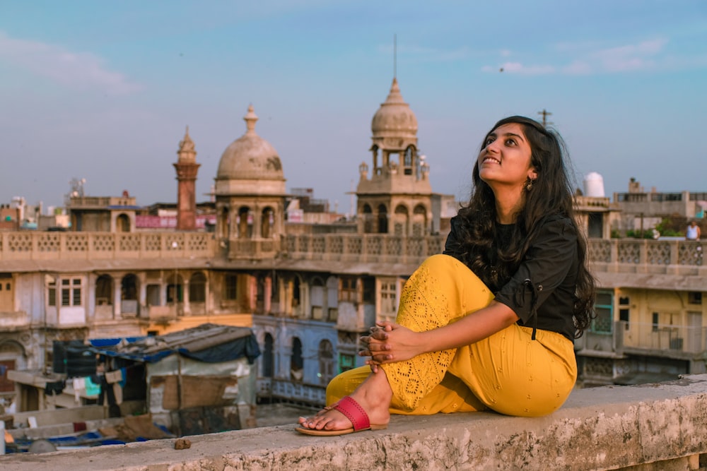 woman in black jacket and yellow pants sitting on concrete floor