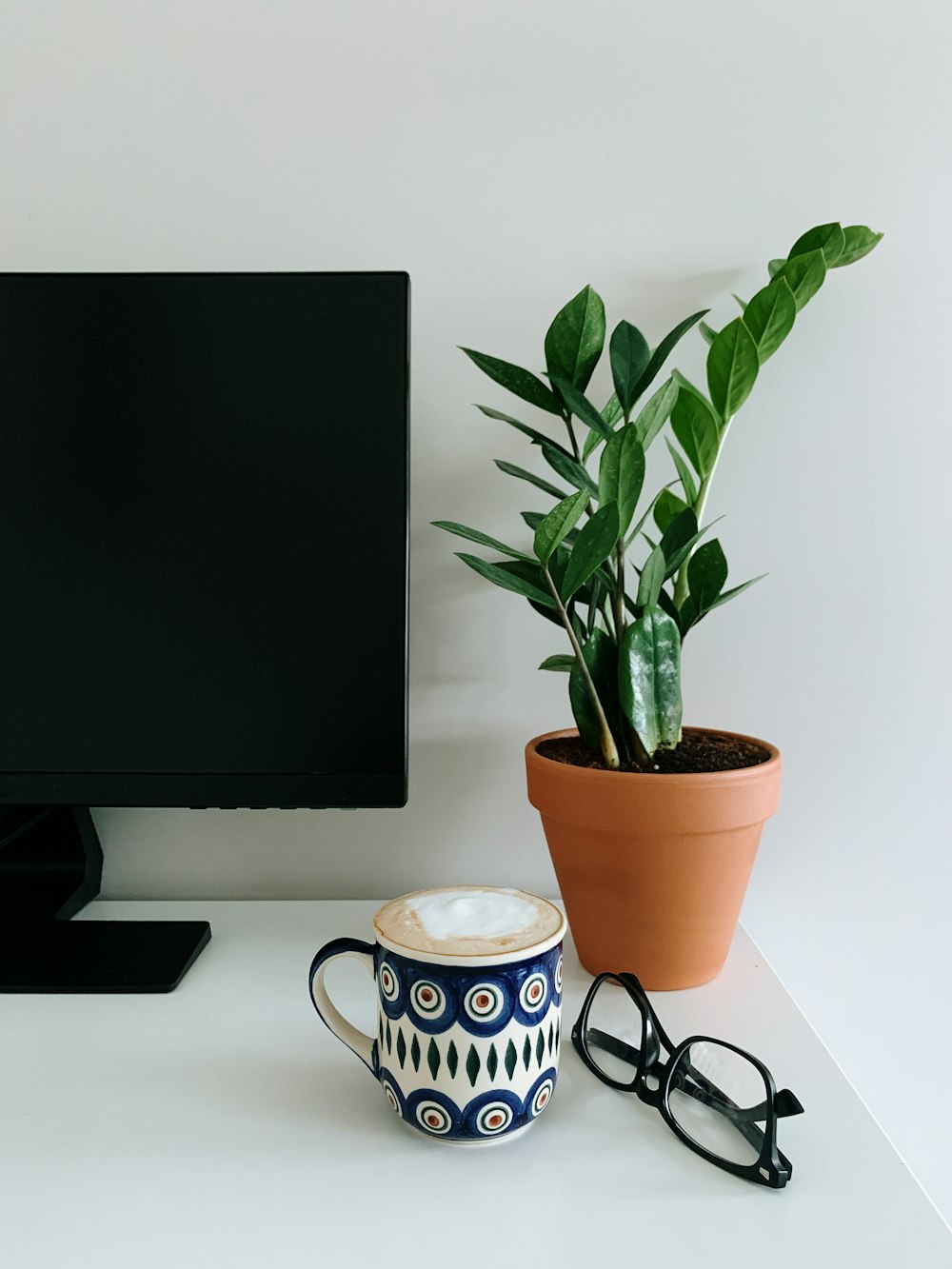 black flat screen computer monitor beside white and blue ceramic mug