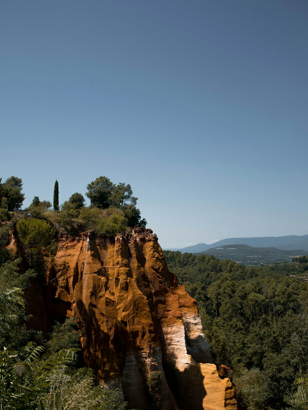 brown rocky mountain with green trees under blue sky during daytime