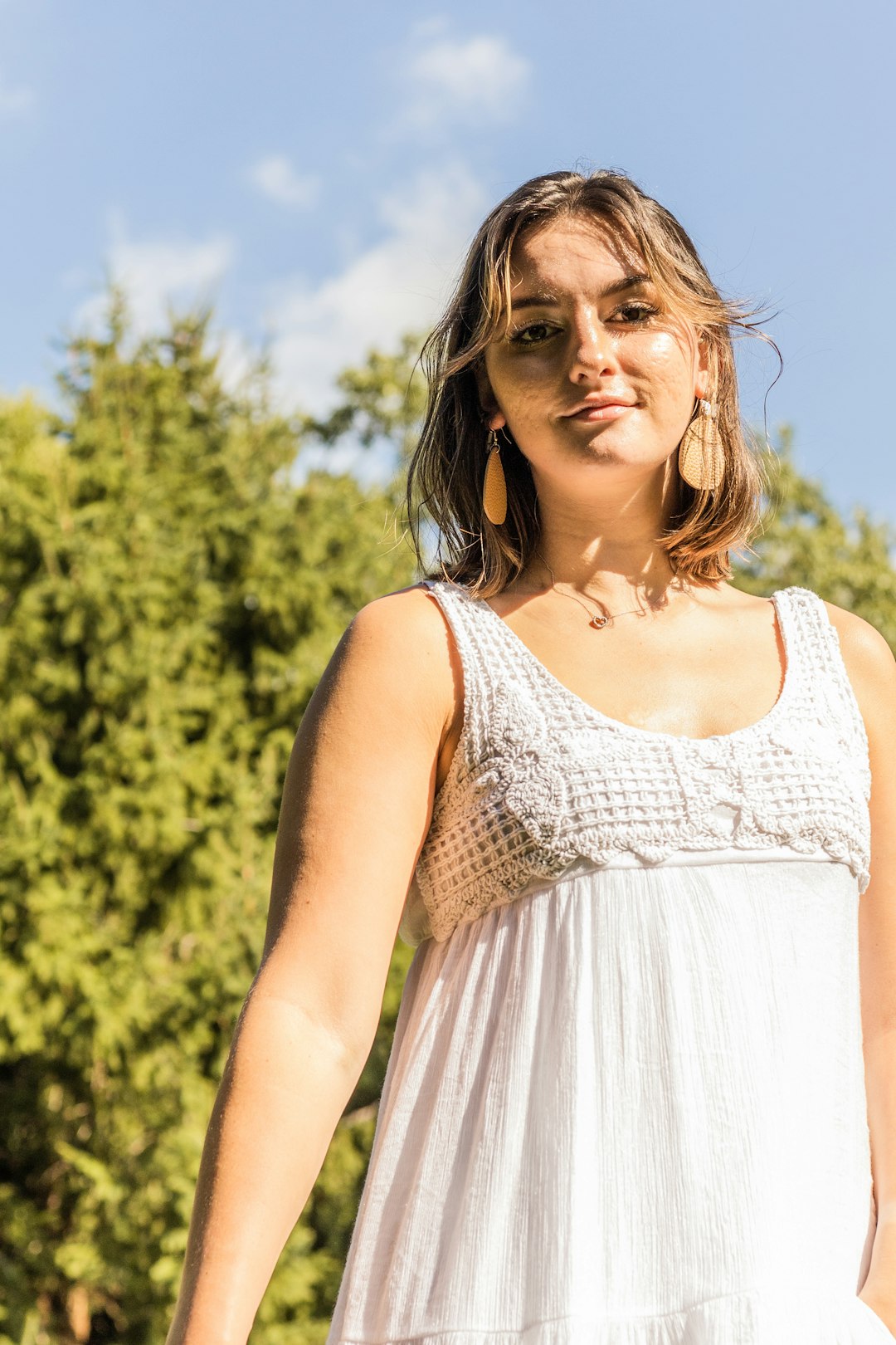 woman in white sleeveless dress standing near green trees during daytime