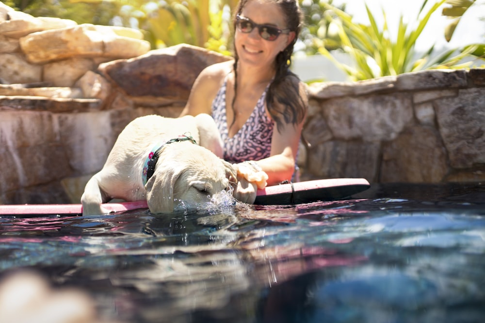 woman in white and red floral tank top sitting beside white short coated dog on water