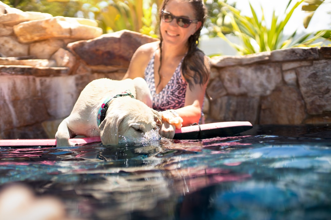 woman in white and red floral tank top sitting beside white short coated dog on water