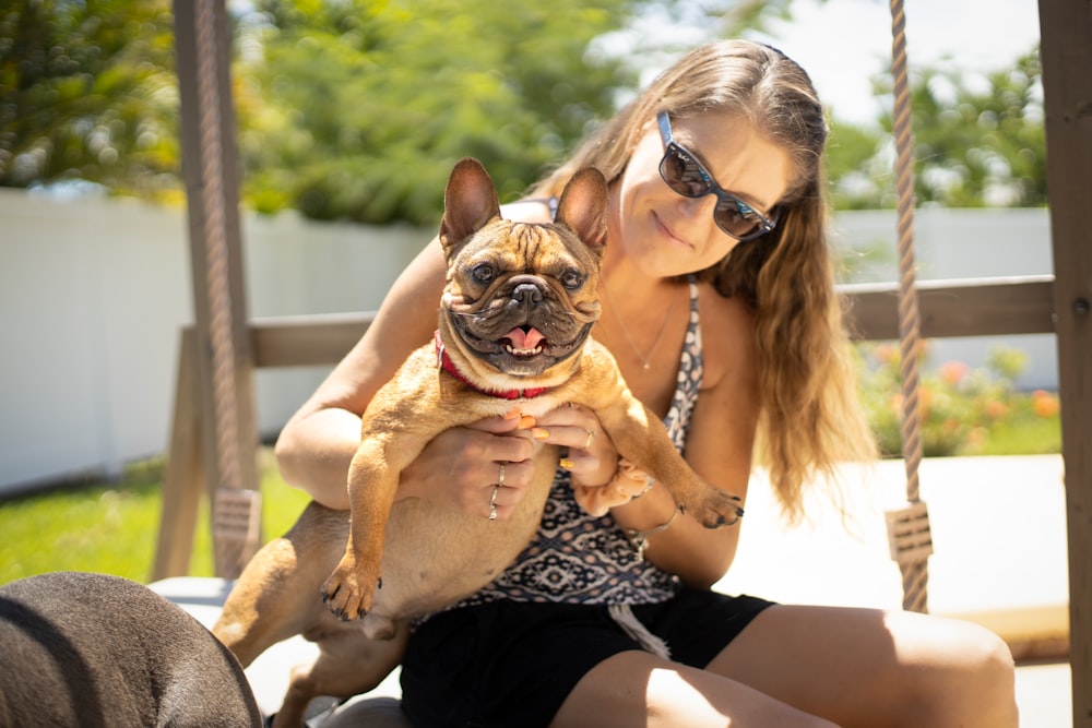 woman in black and white leopard print tank top carrying brown pug