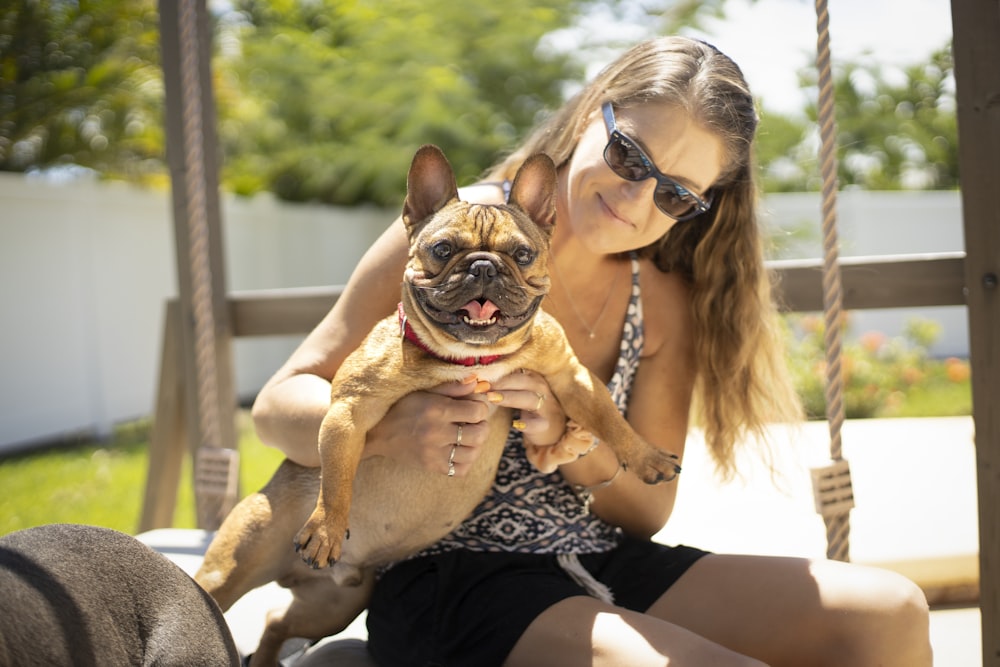 woman in black and white leopard print tank top carrying brown pug