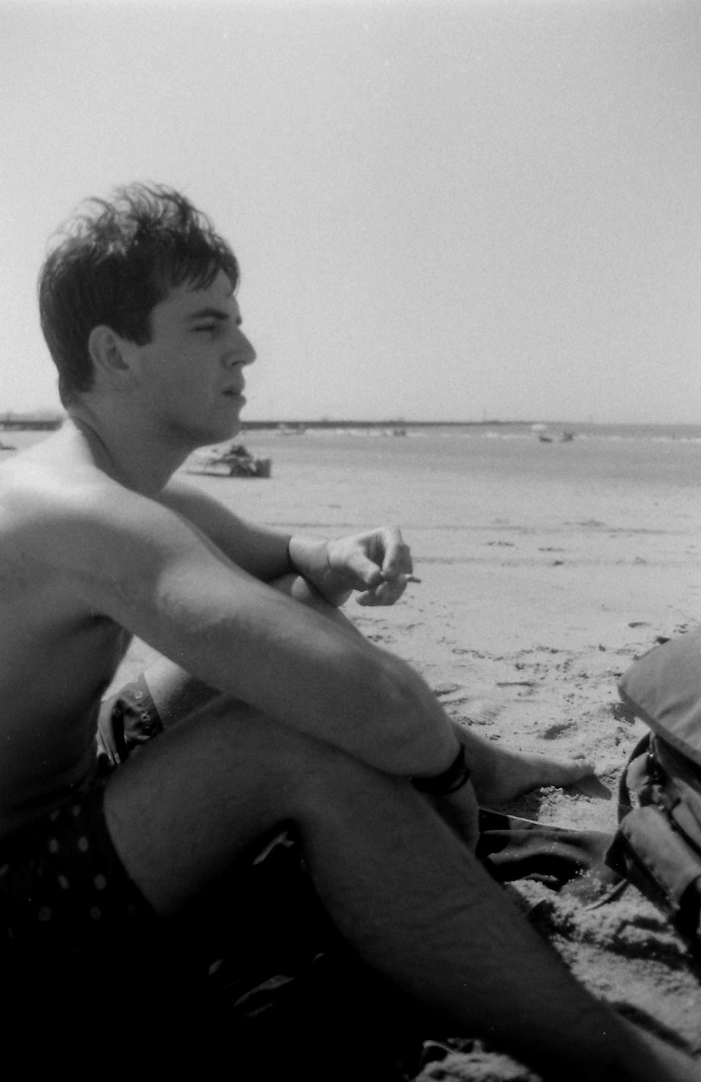 topless boy sitting on beach shore