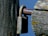 A close-up view of a weathered lock attached to a rusty metal bar. The lock and bar are affixed to an old wooden post, showing signs of age and exposure to the elements with moss and lichen growth. The background is a clear blue sky.